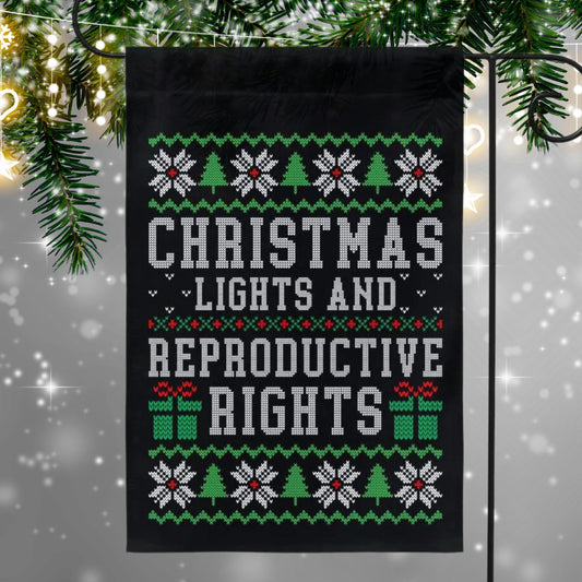 Black garden flag with ugly christmas sweater design. Shows snowflakes, presents, and christmas trees in green and red. Text reads 'christmas lights and reproductive rights'.