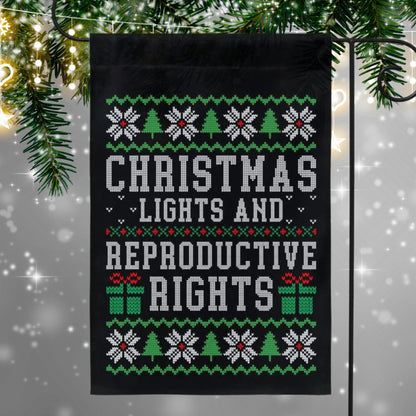 Black garden flag with ugly christmas sweater design. Shows snowflakes, presents, and christmas trees in green and red. Text reads &#39;christmas lights and reproductive rights&#39;.