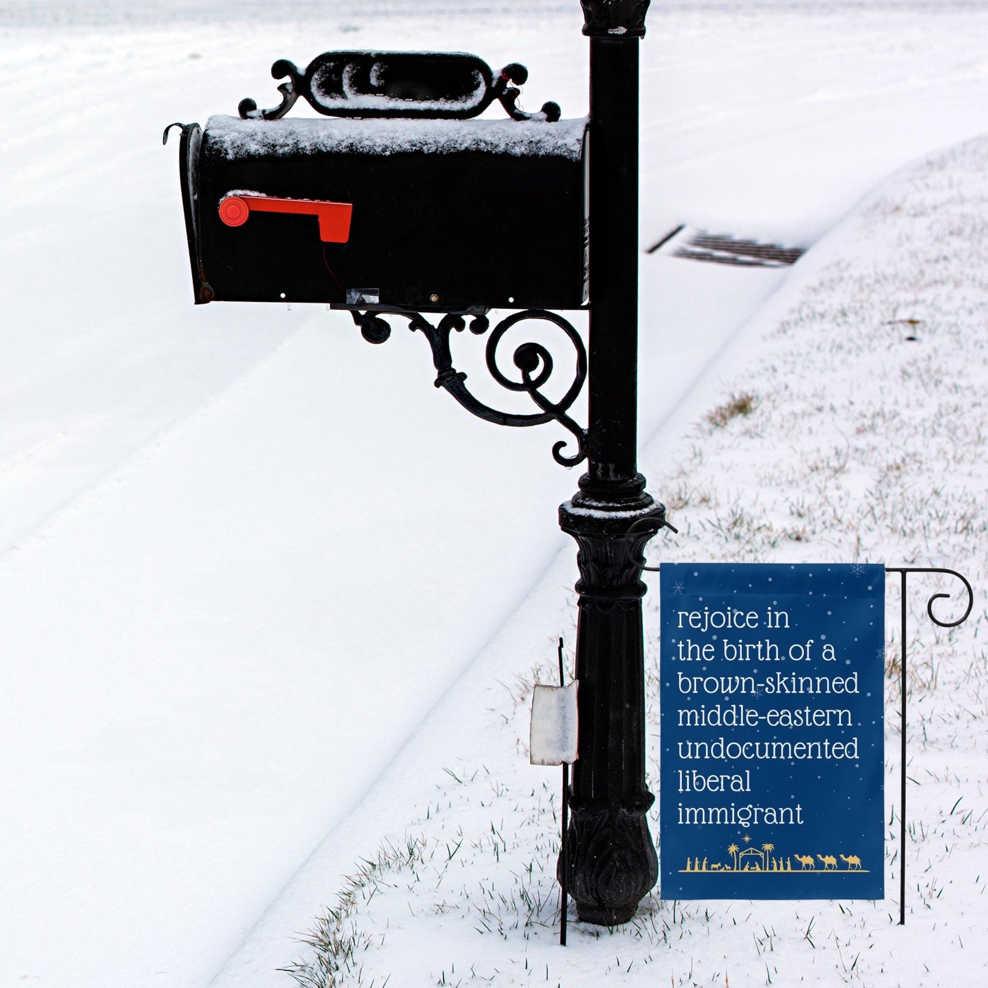 Navy blue garden flag with snow in background and gold manger christmas scene along the bottom. Text reads in white font rejoice in the birth of a brown skinned middle eastern undocumented liberal immigrant
